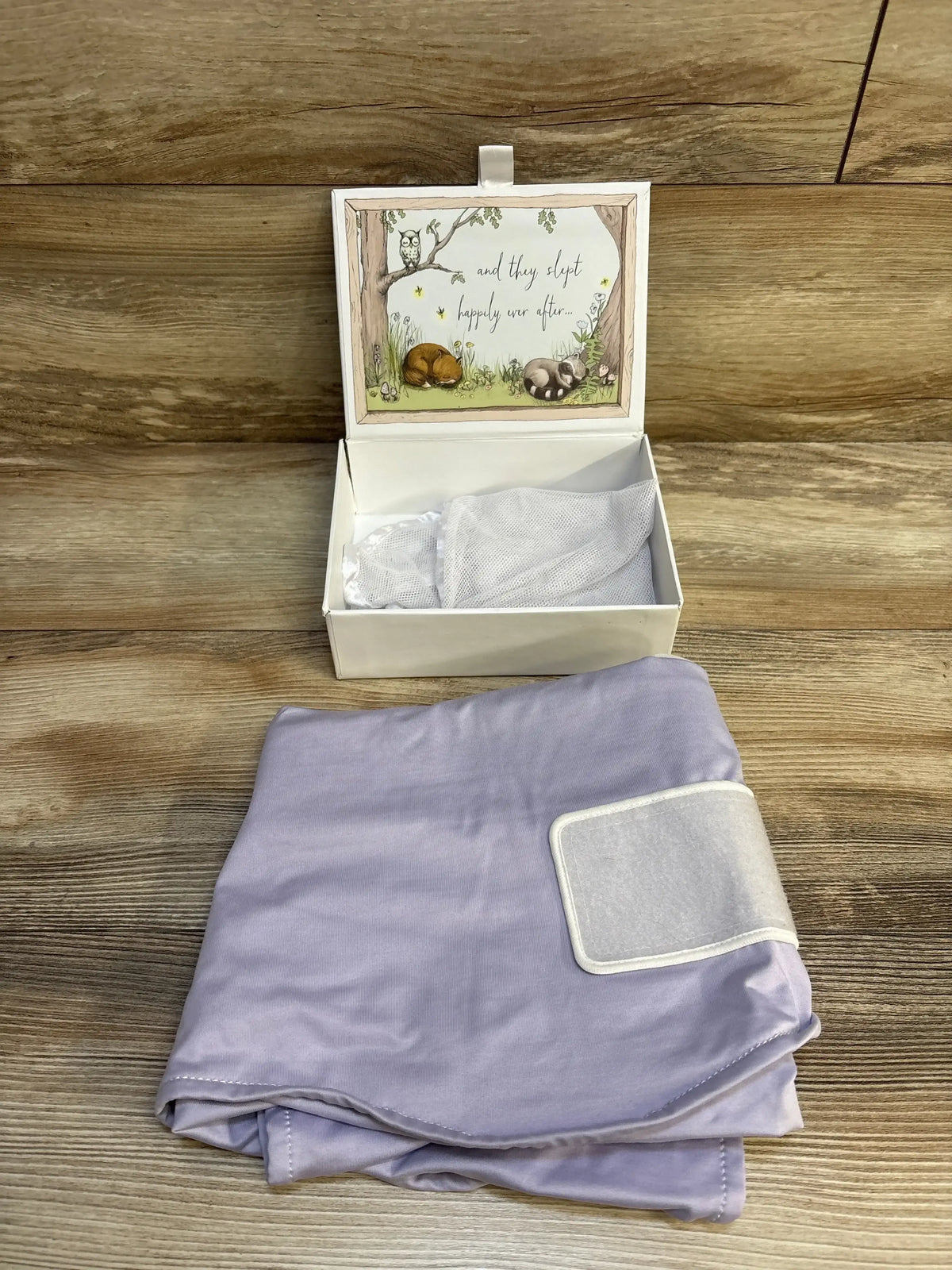 Lavender baby swaddle blanket next to open gift box with woodland animal design