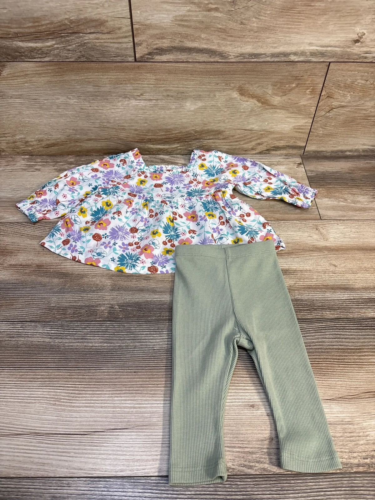 Floral baby top with ruffled sleeves and green ribbed leggings on wood floor