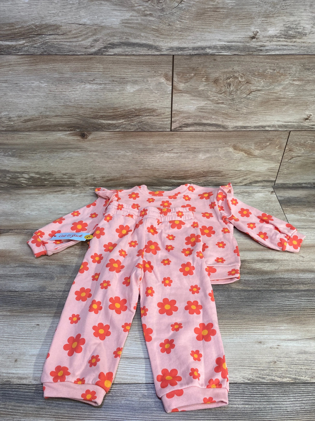 Flat-lay of Cat & Jack toddler 2-piece French terry set in peach with orange flower print showcasing elastic-waist pants and long-sleeve ruffle-top on wood background