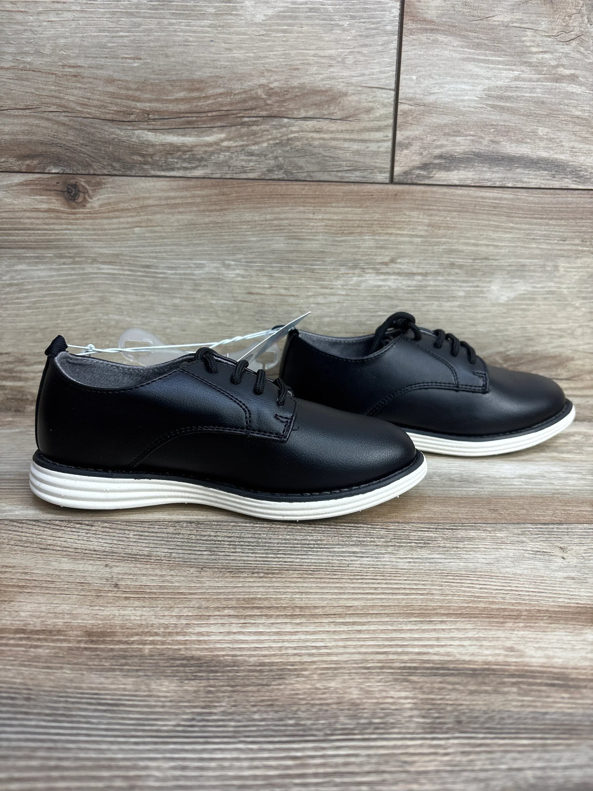 Side view of Cat and Jack Alfi kids black lace-up dress shoes showcasing white ridged rubber sole on wooden background