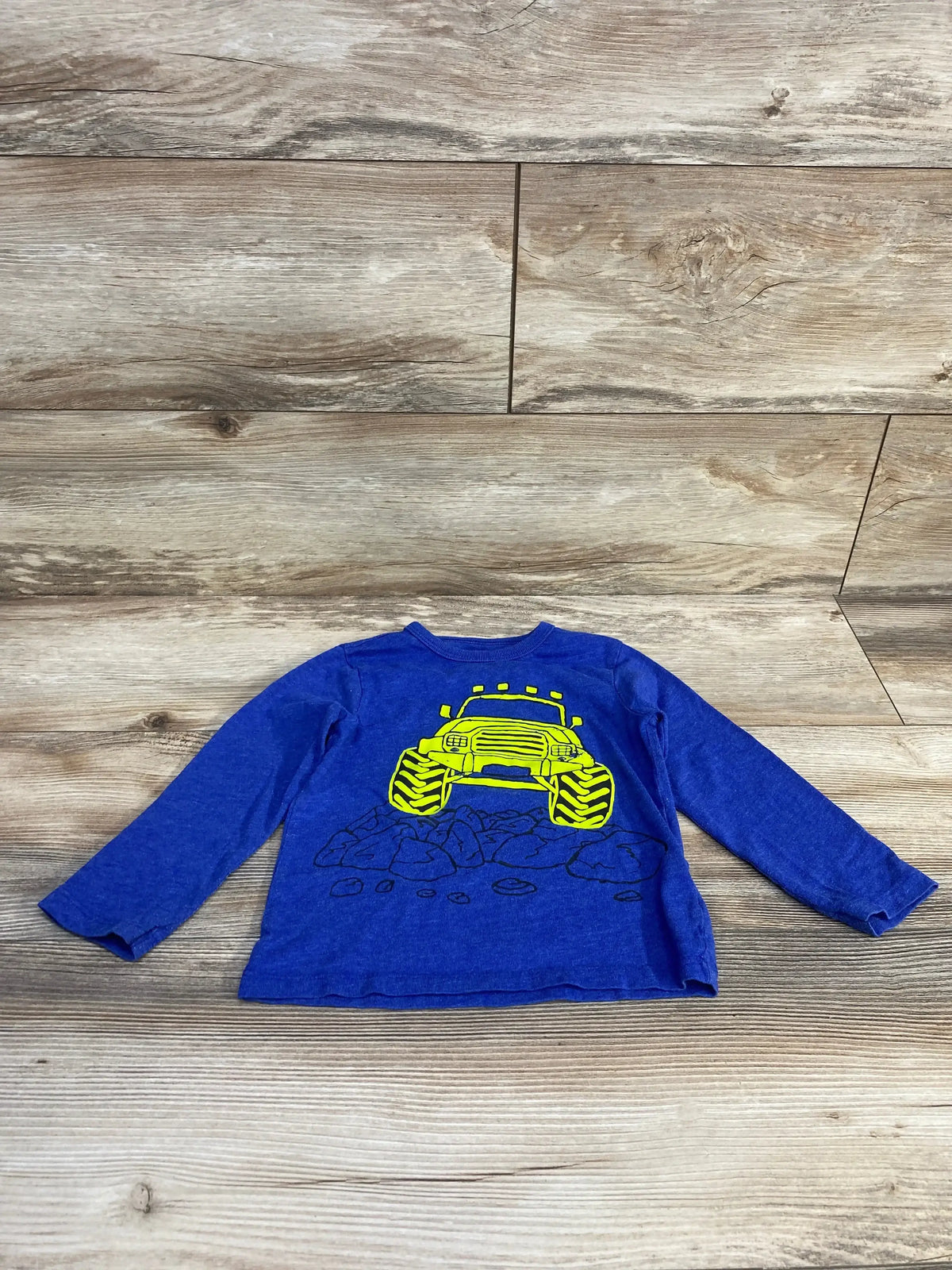 Front view of Children’s Place blue long-sleeve toddler shirt 2T with yellow monster truck graphic on wooden background