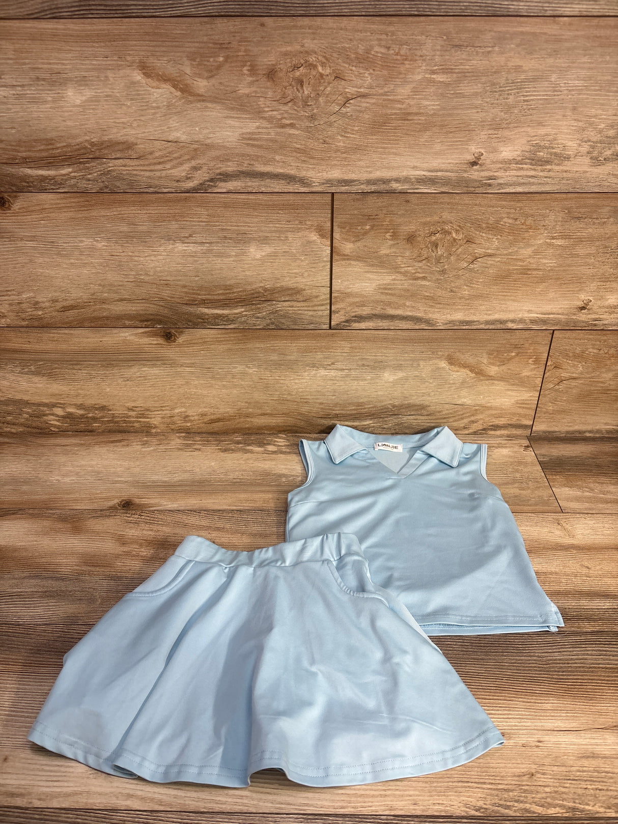 Flat lay of blue 2-piece girls' tennis outfit, collared sleeveless top and flared skirt with elastic waist on wood background