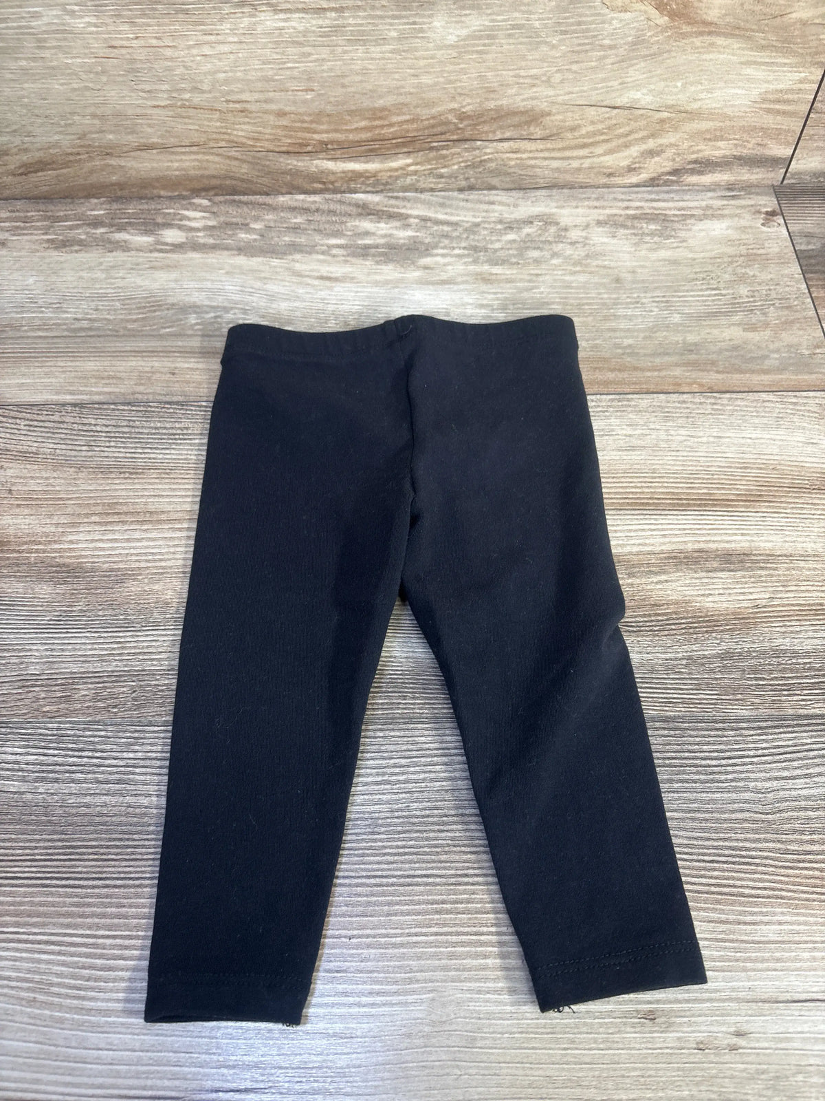 Front view of Jumping Beans black cotton leggings for 12 months showcasing elastic waistband on a wood-look floor