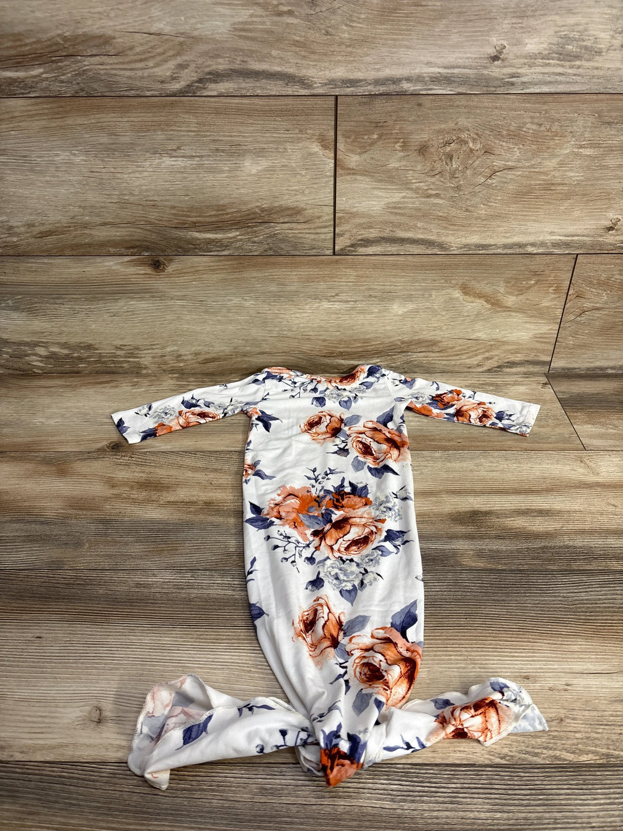 Floral print baby gown with long sleeves, peach and navy flowers on white, laid on wood floor