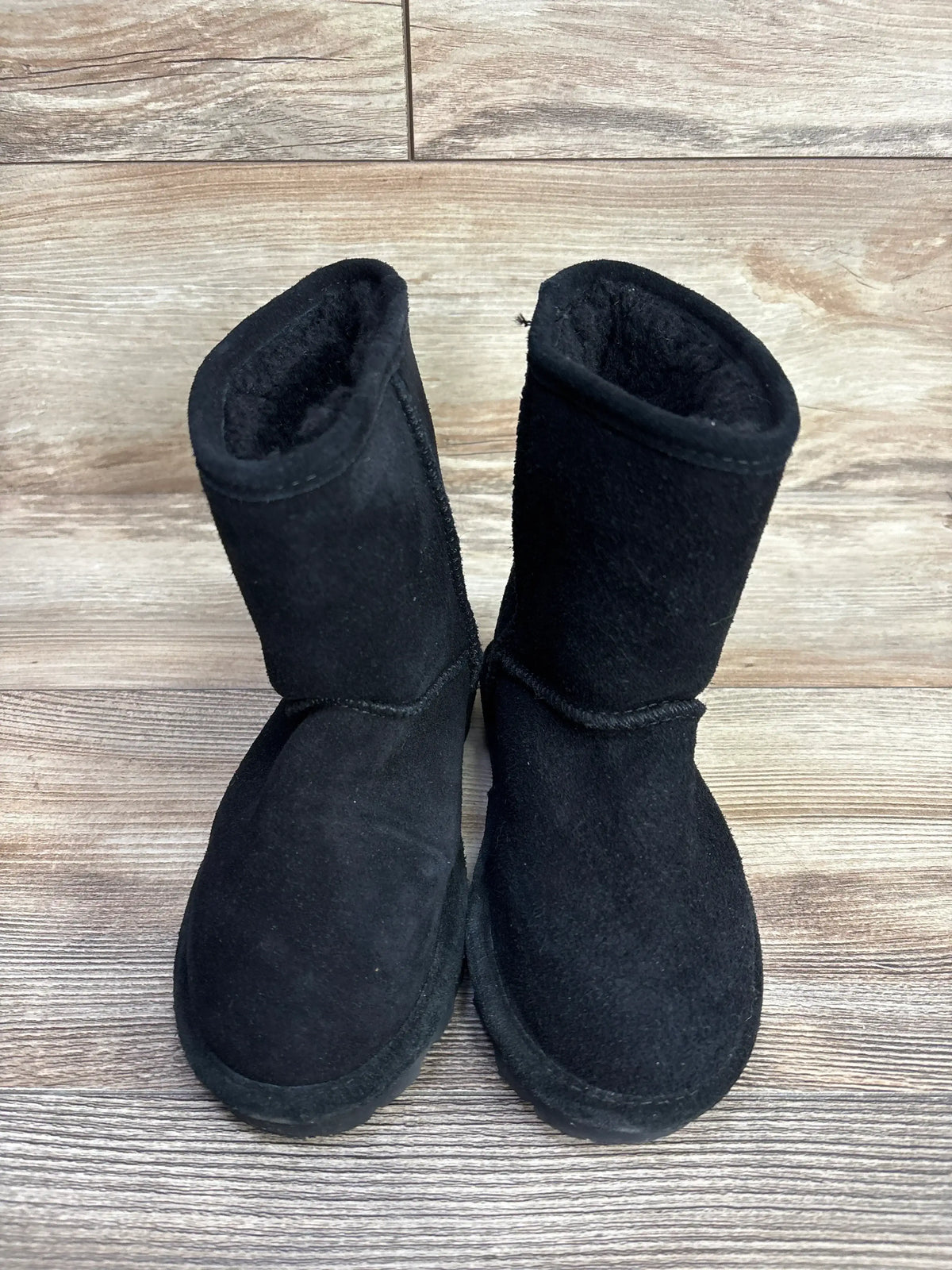 Pair of black toddler winter boots with plush lining on wooden floor background