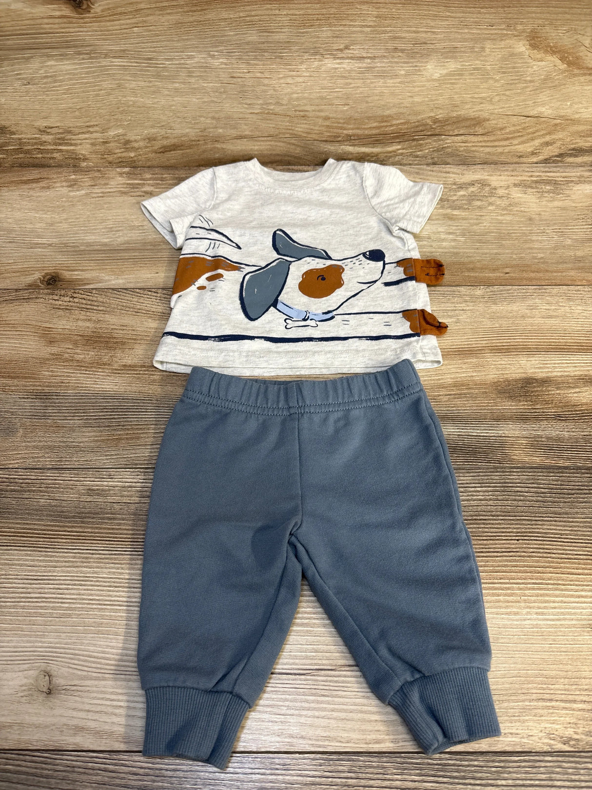 Flat lay of Carter's grey short-sleeve dog graphic t-shirt and blue jogger pants (3M) showing front dog print and elastic waistband on wood background
