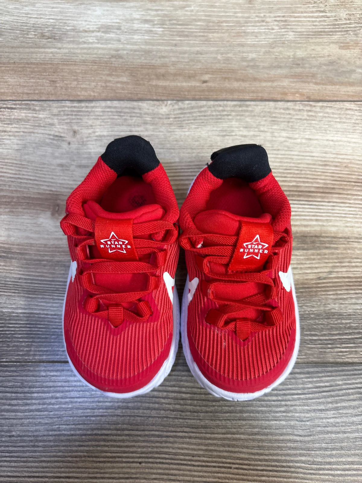 Top view of toddler Nike Star Runner 4 sneakers showcasing University Red mesh uppers, white swooshes, and white soles on wood