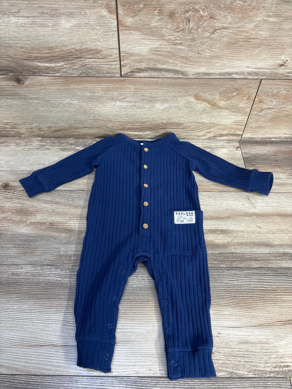 Flat lay of blue ribbed baby coverall size 9 months with front wooden buttons, Explore More chest patch, and snap leg closures