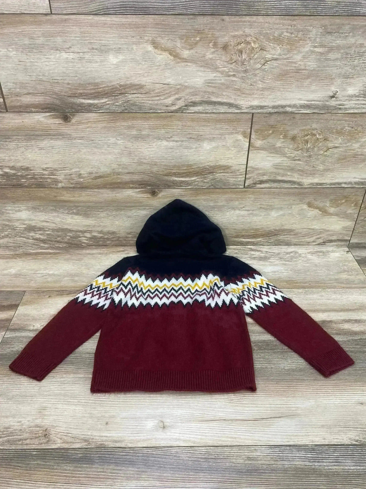 Flat-lay of Mayoral toddler knit hoodie showing navy hood, burgundy body and zigzag white-and-yellow yoke on wood floor