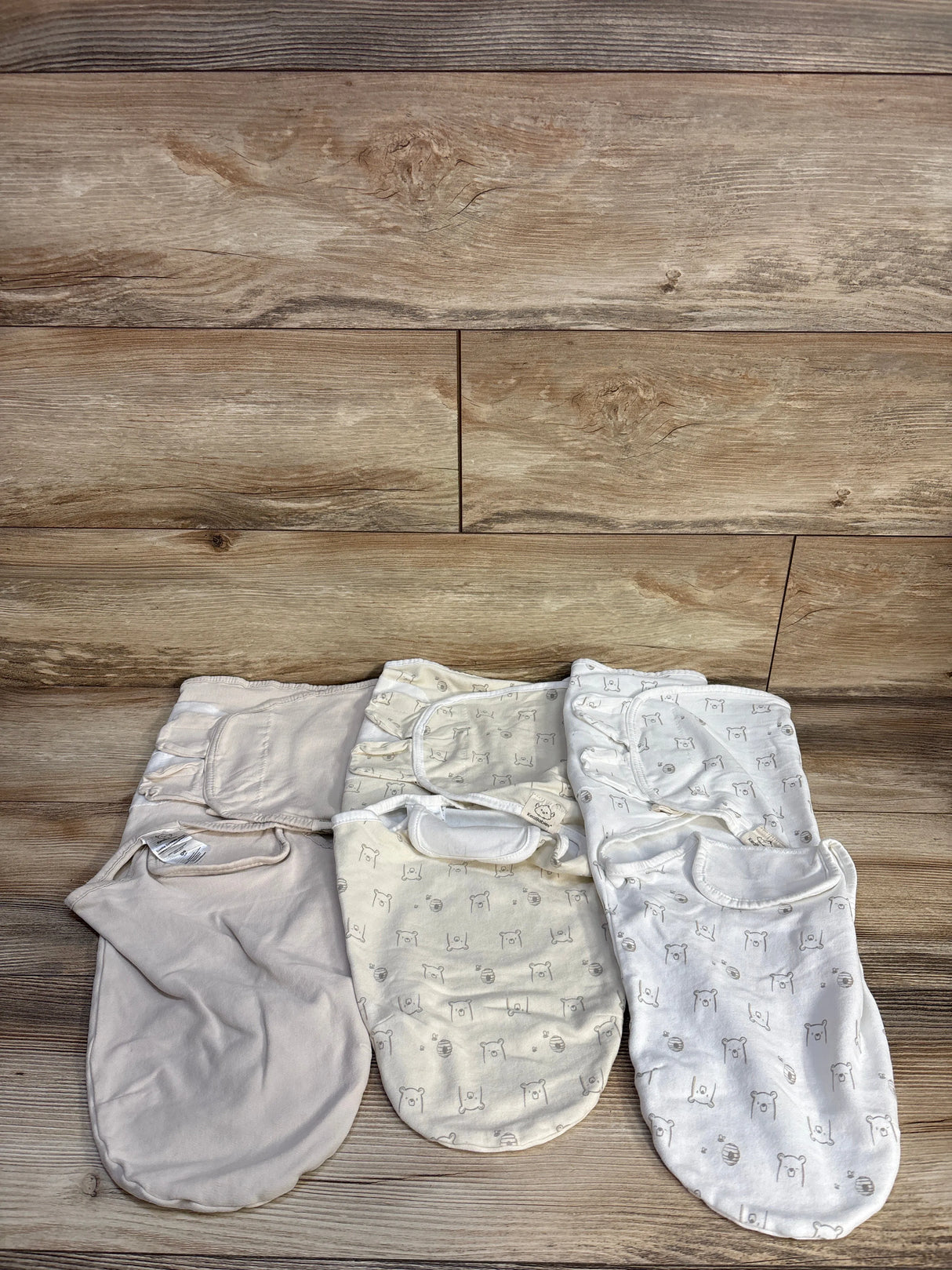 Top-down view of KeaBabies 3-pack newborn swaddles showing two bear-print and one solid beige swaddle laid flat on a wood background
