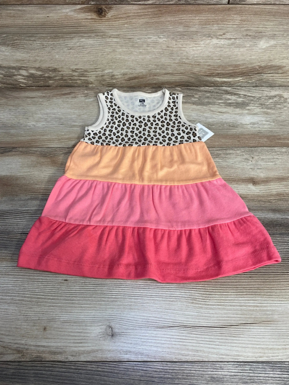 Flat lay of Hudson Baby tank tiered dress with leopard print bodice and three peach to coral tiers on a light wood background