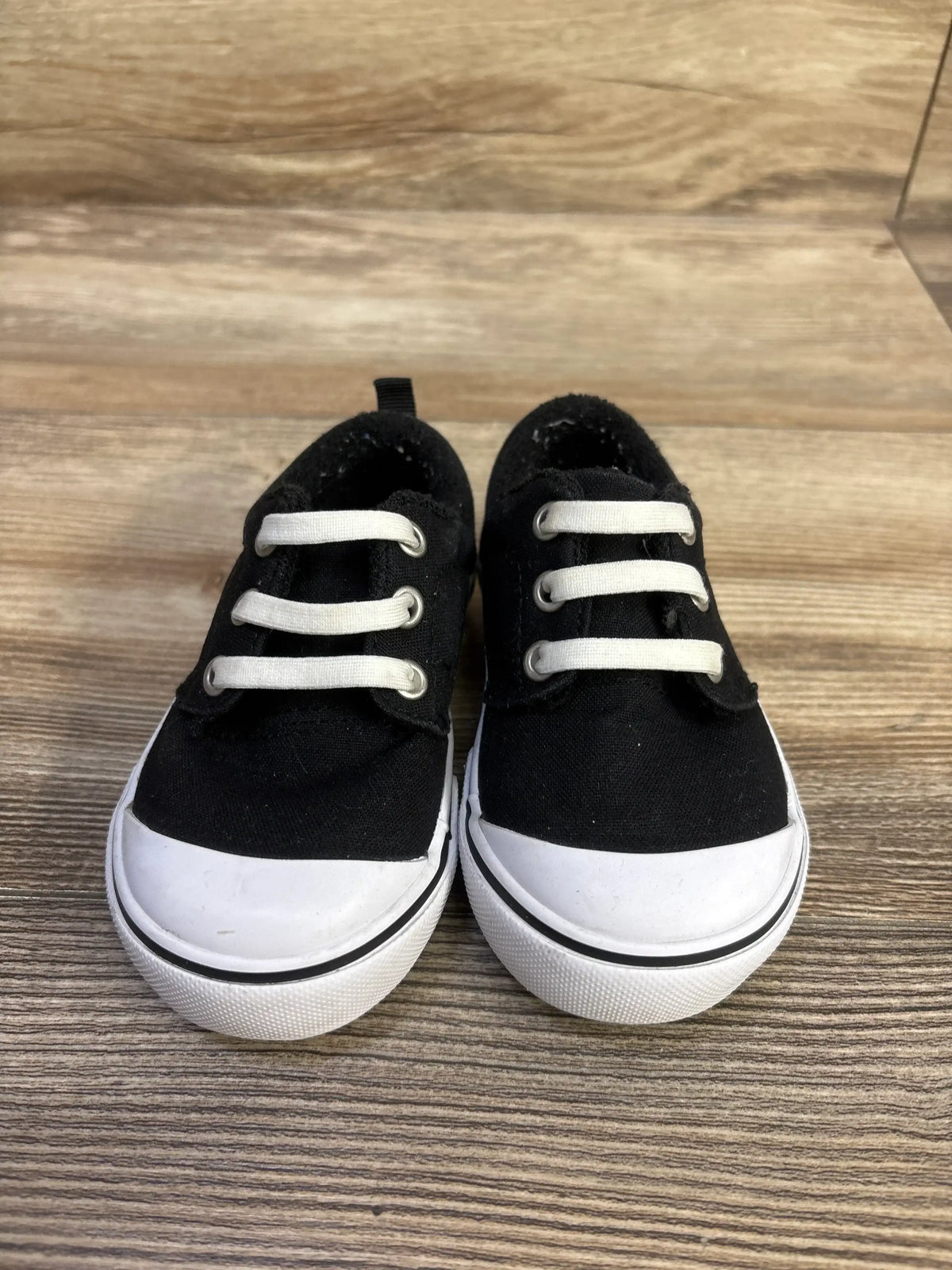 Front view of Wonder Nation canvas bump-toe toddler sneakers in black showing white rubber toe caps and elastic laces on wood background
