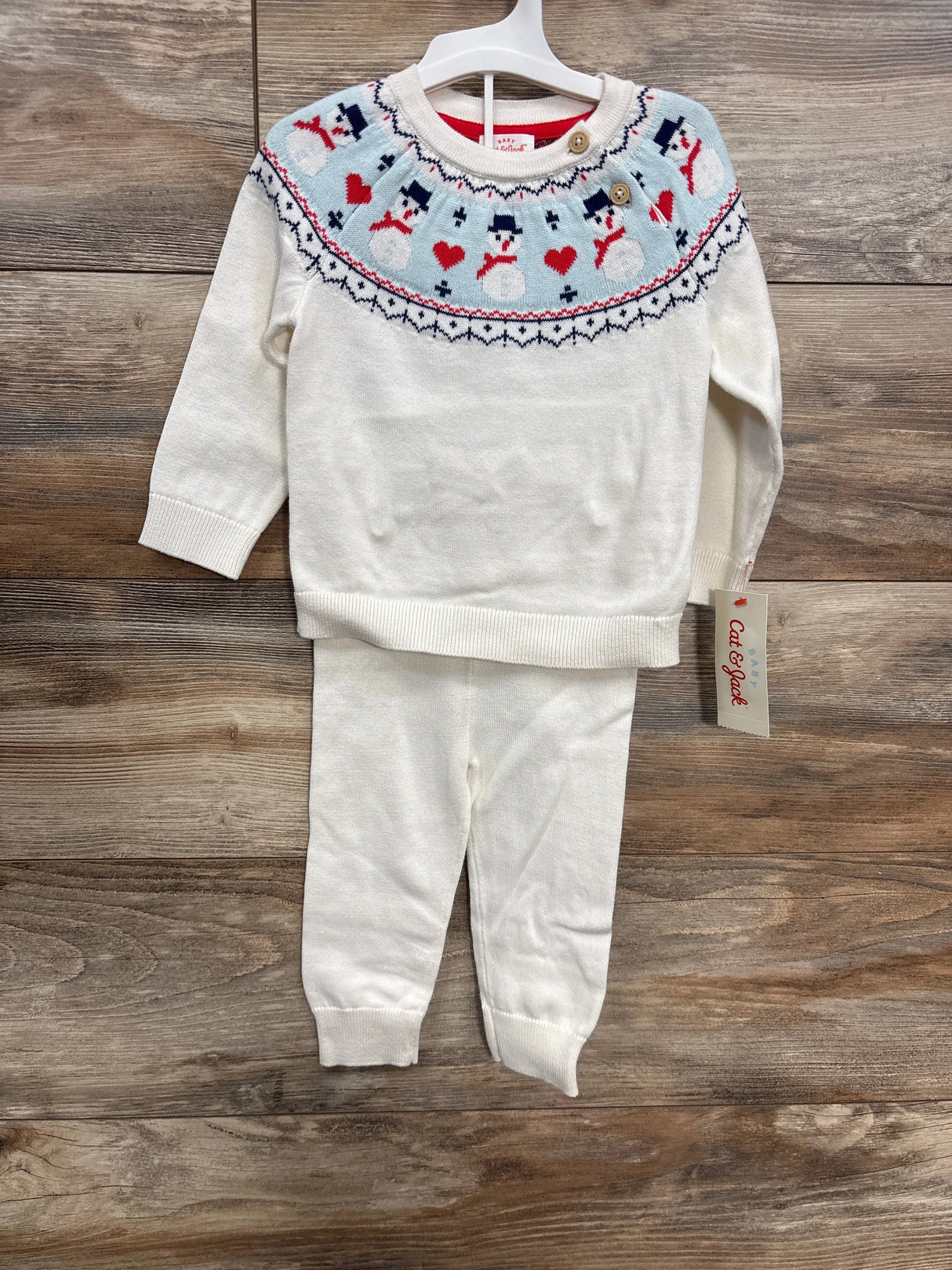 Baby winter sweater and pants set with snowman and heart pattern on wooden background