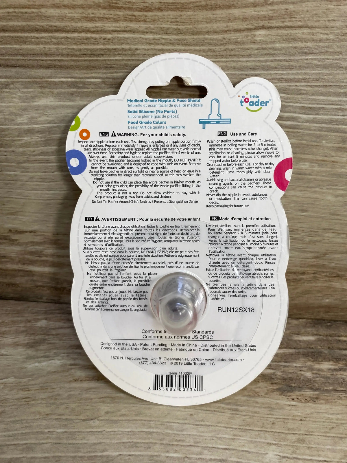 Back view of Little Toader Cupcake pacifier package showing clear silicone nipple and printed care instructions on wooden background