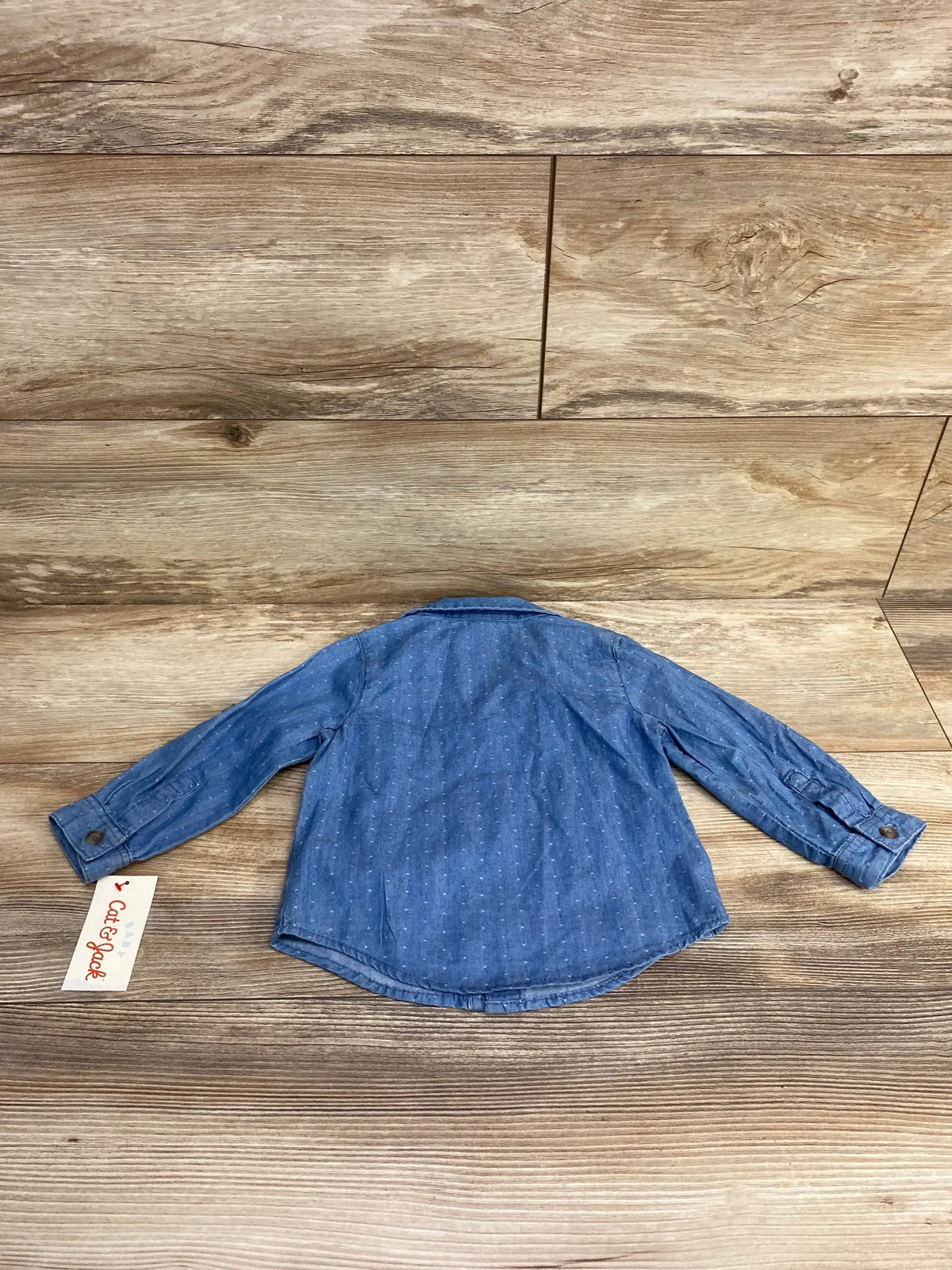 Blue long sleeve toddler denim shirt with subtle polka dots, displayed on wood surface