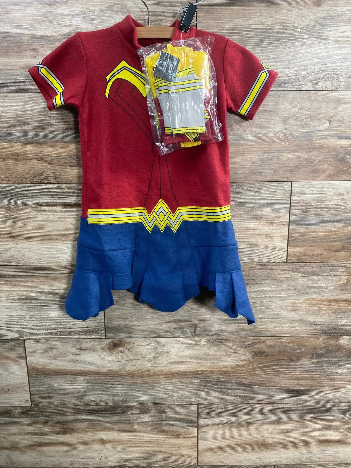 Front view of Justice League Wonder Woman costume set in red and blue with gold trim and emblem, plus packaged accessory