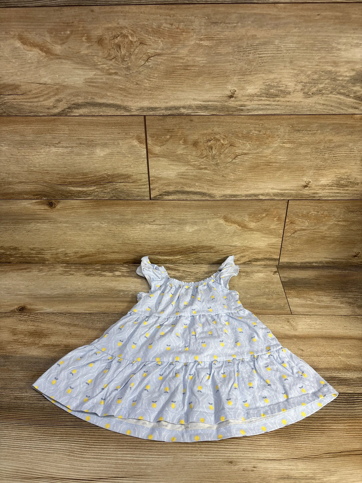 Flat lay of Just One You blue and white striped sleeveless tiered dress with yellow heart print on wood plank floor