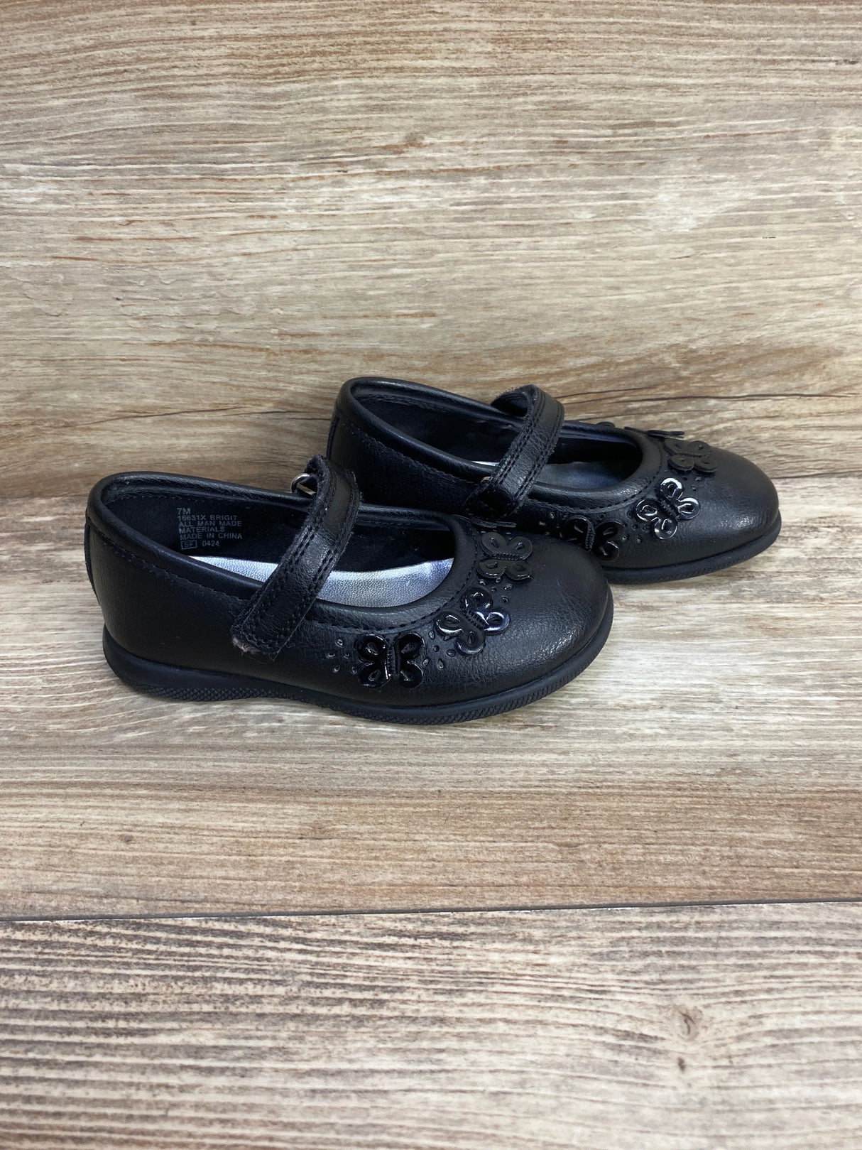 Black toddler Mary Jane shoes with butterfly accents on wood background