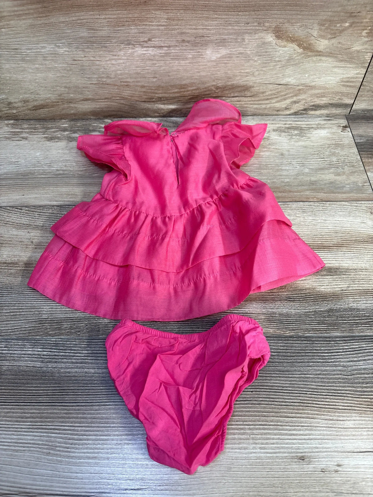 Top view of newborn pink Cat & Jack flutter-sleeve dress with tiered ruffles and matching diaper cover on wood background