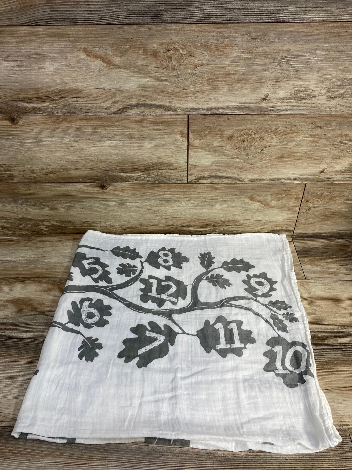 White fabric with gray leaf patterns and numbers 5 to 12 printed, folded on wooden floor