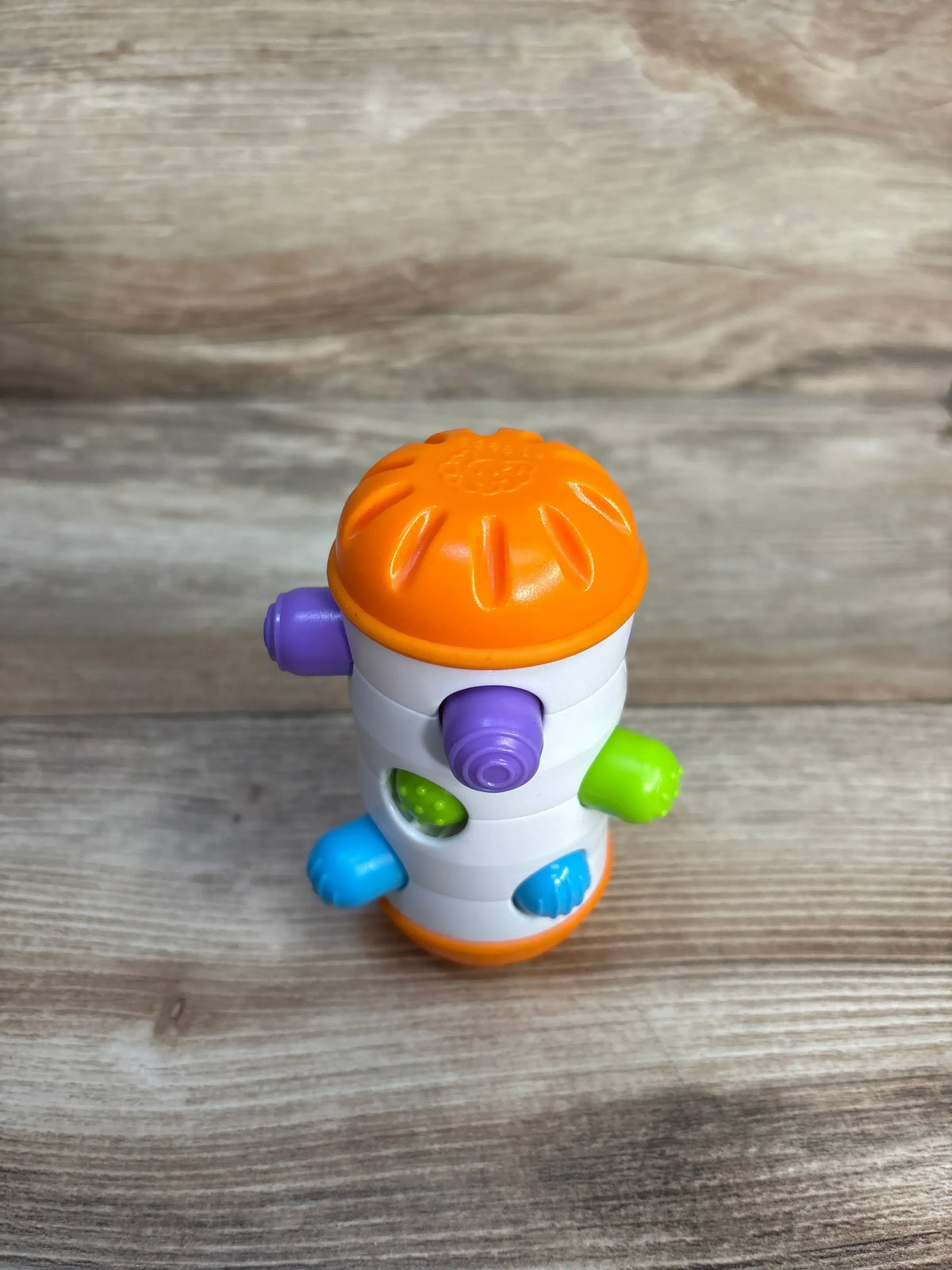Front view of Fat Brain Toys Rolio Rattle showcasing colorful textured pegs and orange top on a wood-grain background