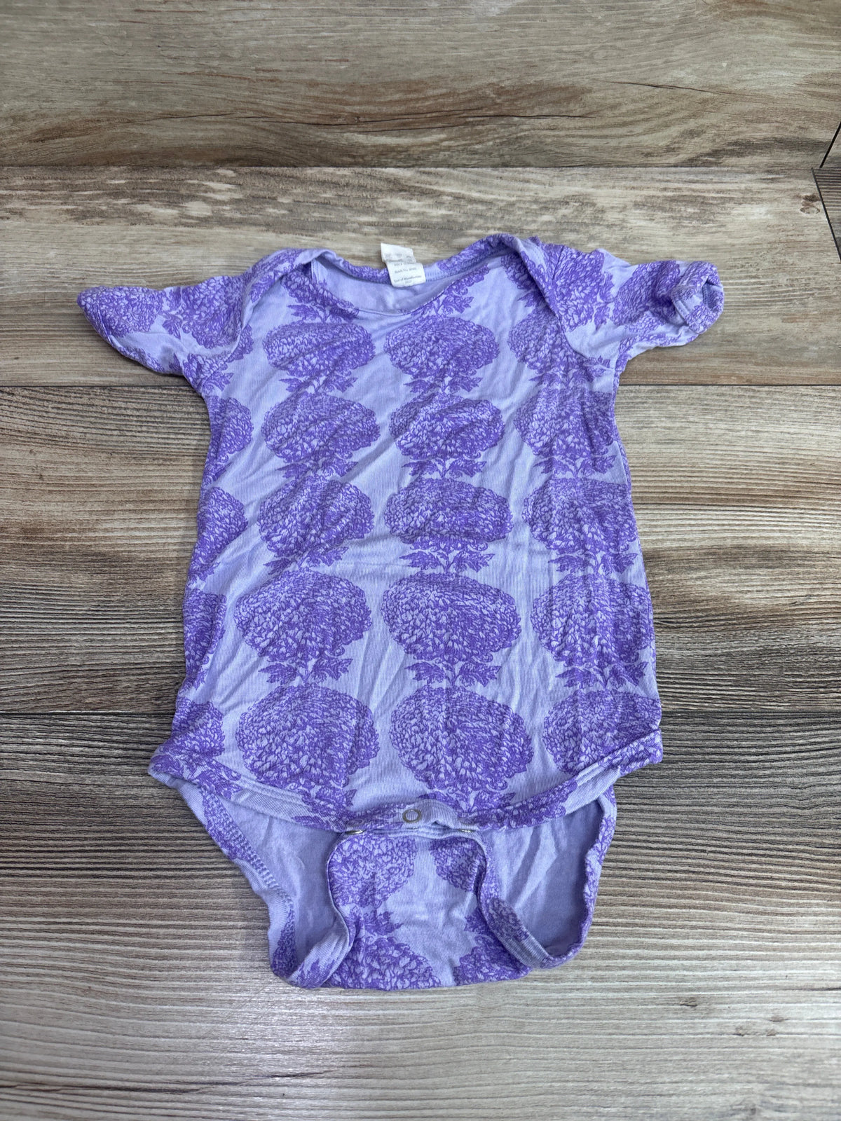 Front view of Kate Quinn bamboo bodysuit in purple, size 6-12m, showcasing a floral pattern on a wood-grain background
