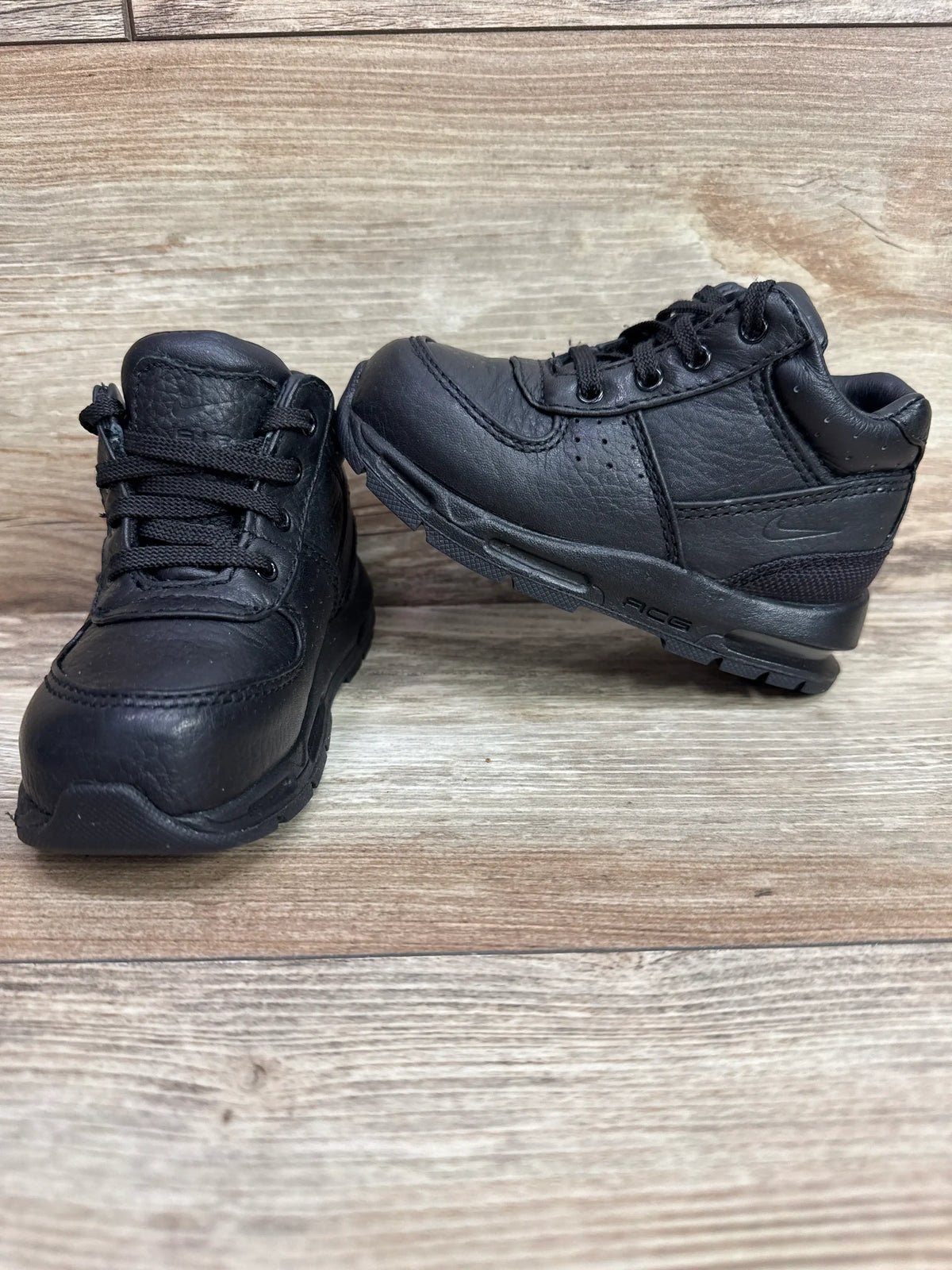 Front and side views of black Nike Air Max Goadome boots with laces and textured soles on a wood surface