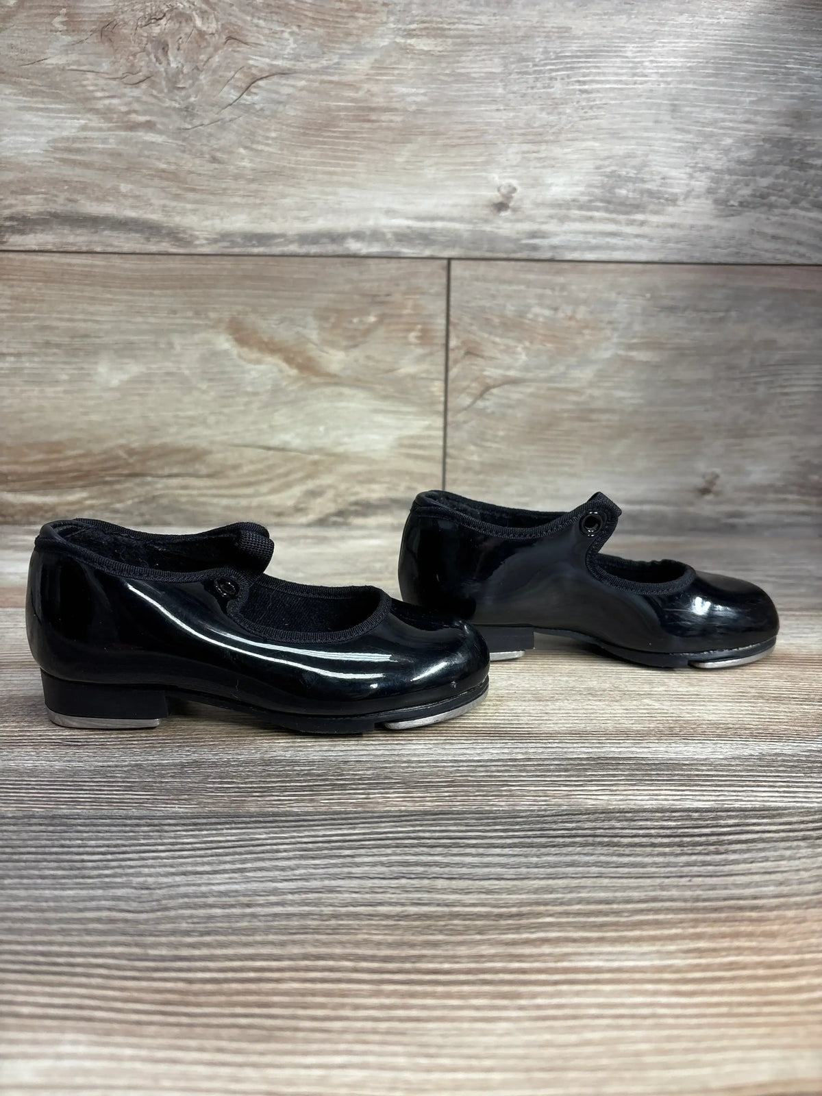 Black patent leather tap shoes with straps on wood background
