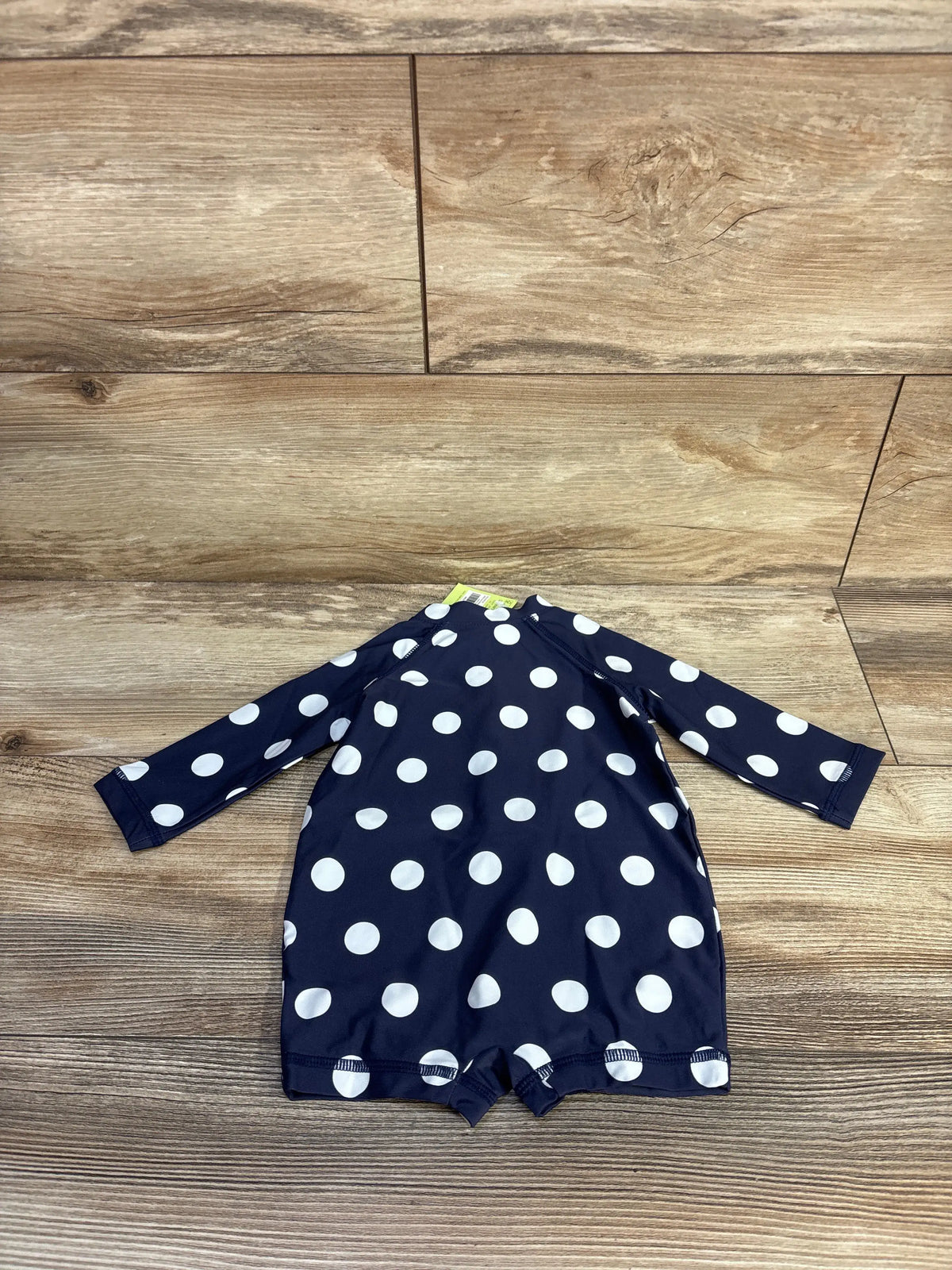 Front view of Primary navy rash guard romper showcasing white polka dots and long sleeves on a wood surface