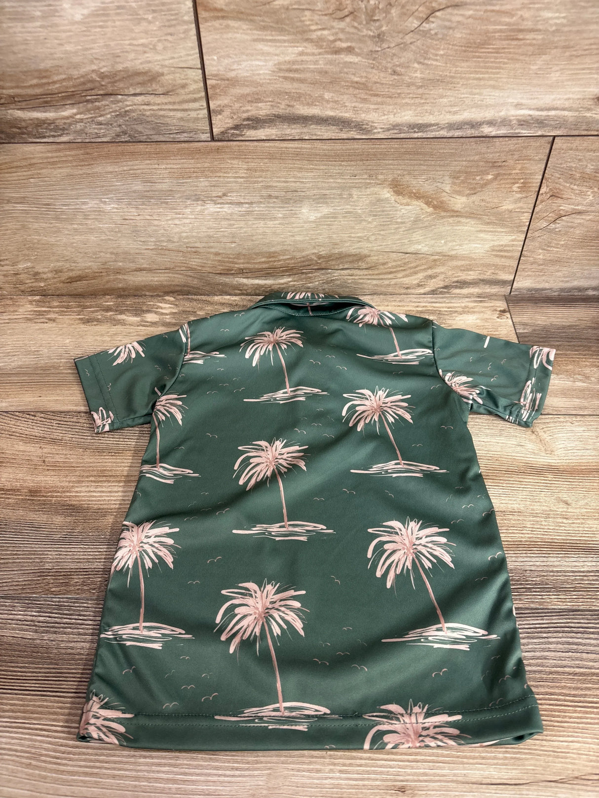 Back view of Hamakua Keiki green polo shirt (3T) showing pink palm tree print, short sleeves, and camp collar on wood floor