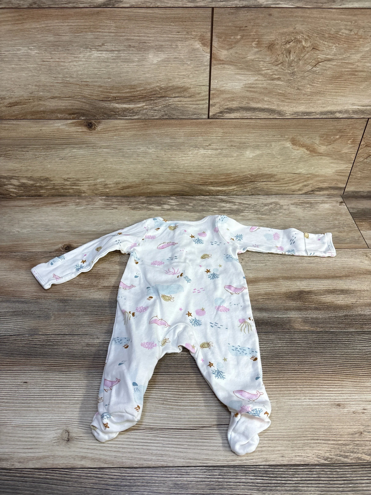Flat lay of white footed baby sleeper with pastel ocean print showing whales, shells, and starfish, size 3M on wood background