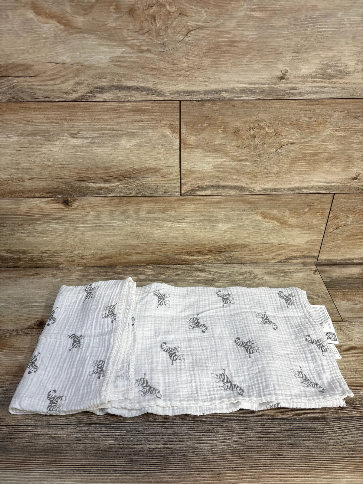 Top view of Amazing Baby muslin swaddle blanket showing black zebra print on white fabric on a wood floor