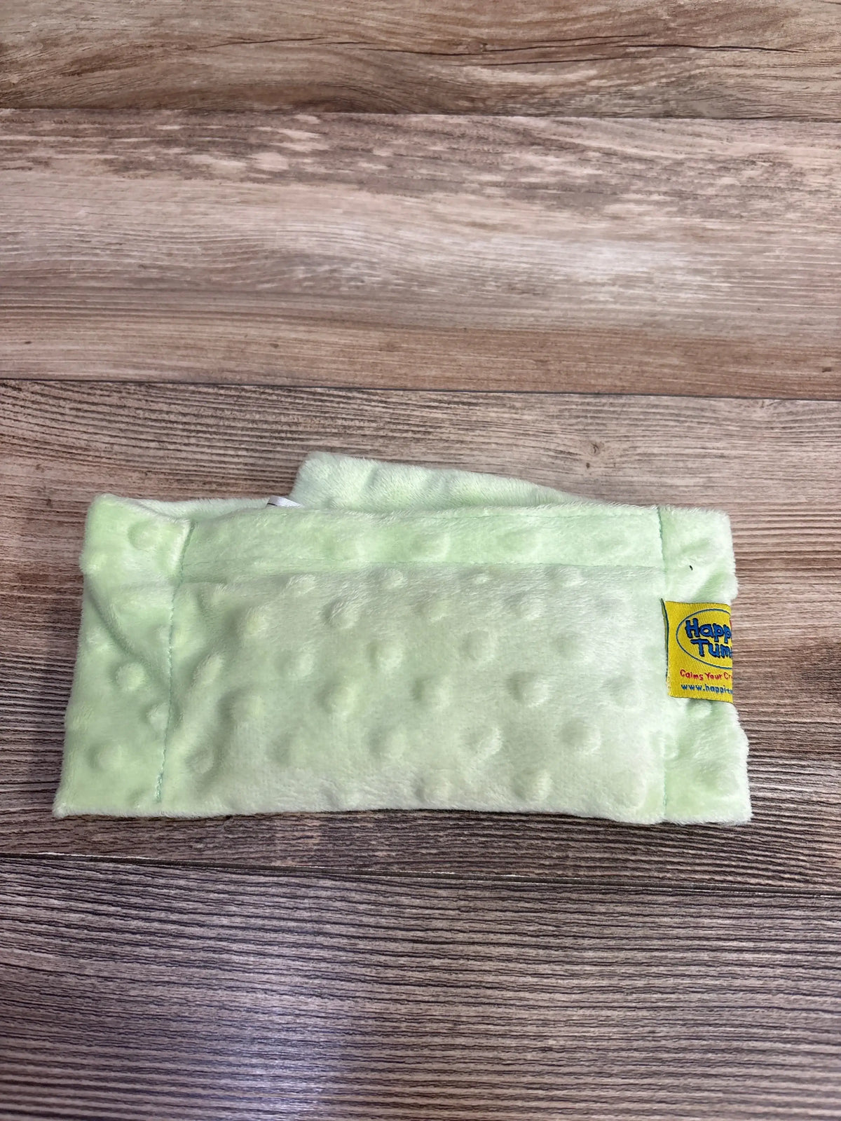 Top-down view of Happi Tummi colic and gas relief waistband, light green minky with dimpled texture and yellow tag on wood