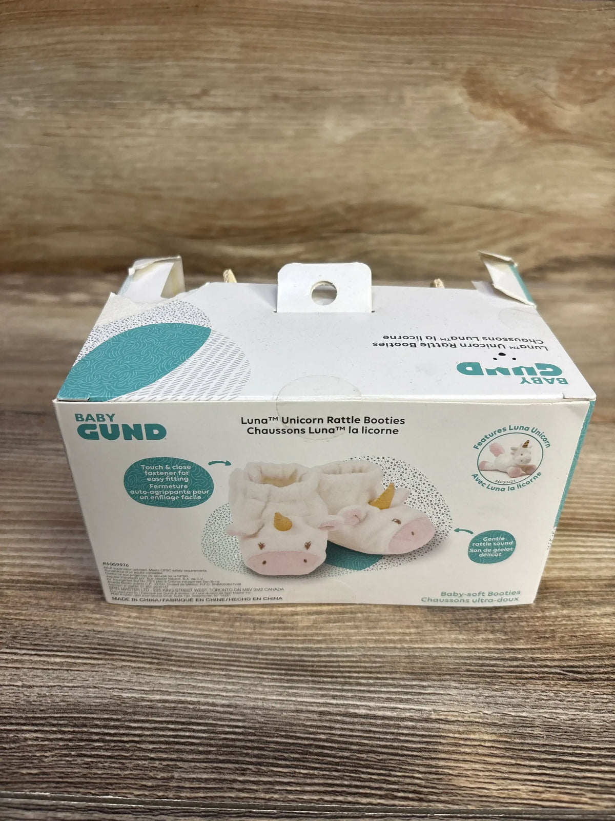 Front-top view of Baby GUND Luna Unicorn plush rattle booties box showing picture of white unicorn booties on wood tabletop