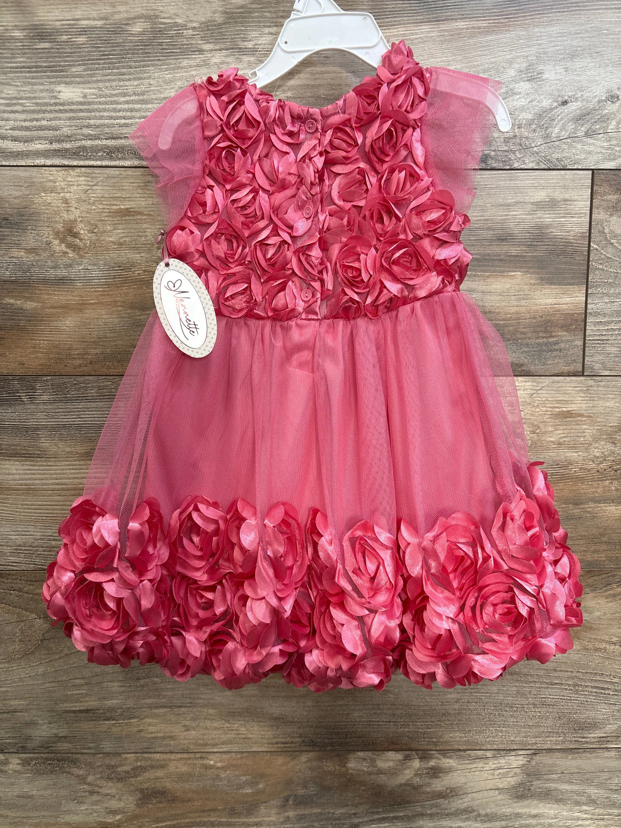 Front view of pink toddler rosette dress, size 3T; satin rosette bodice and layered skirt on white hanger on wood background