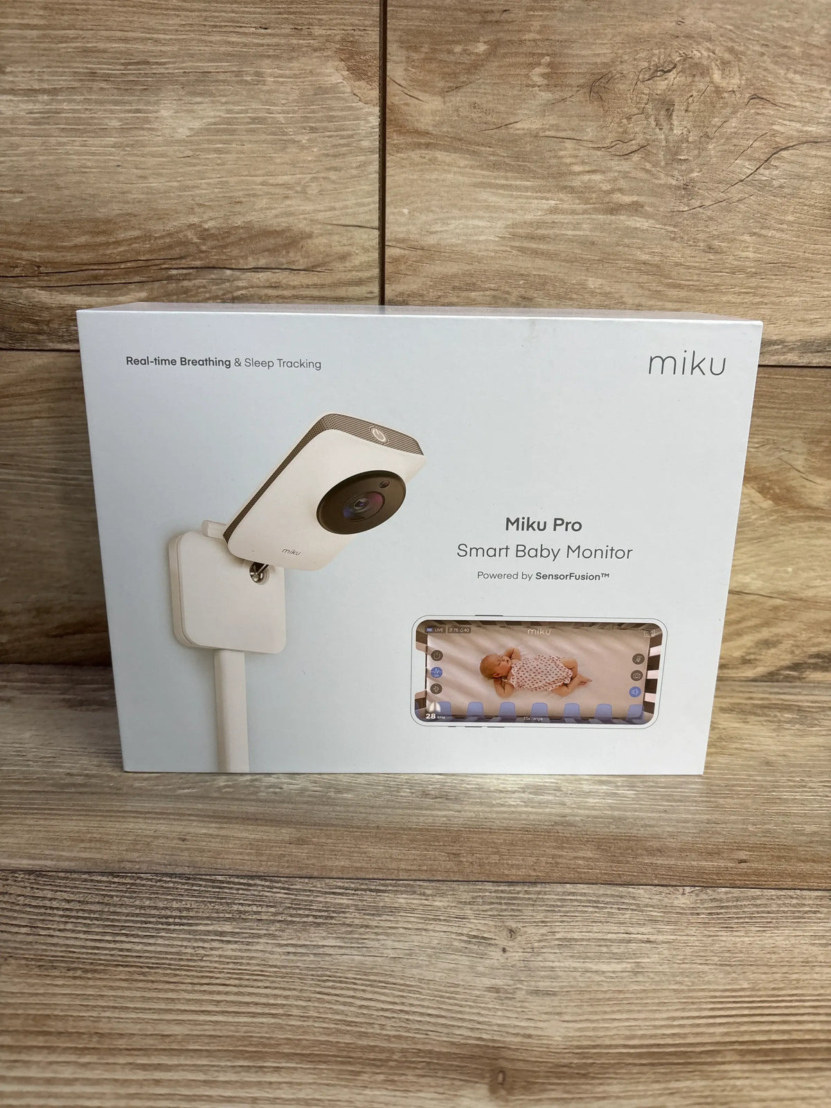 Front view of Miku Pro Smart Baby Monitor with wall mount kit box showing real-time breathing and sleep tracking on wood floor