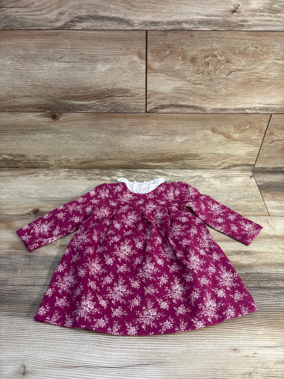 Flat-lay front of Janie & Jack long-sleeve quilted pink baby dress with white floral print and ruffled collar on wood