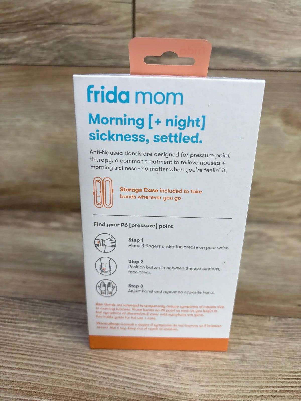 Back view of Frida Mom Anti-Nausea Bands 2-count showing headline Morning and night sickness, settled and P6 pressure-point instructions on a wood background