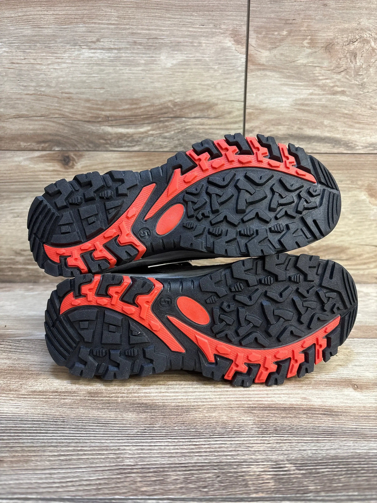 Sole view of Cat & Jack Patsy hiking boots size 5Y showing black soles with red tread accents and rugged lug pattern on wood floor