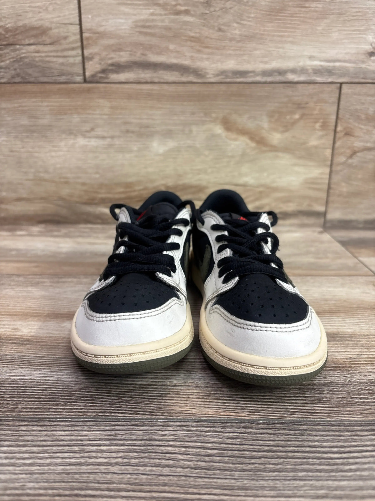 Front view of Travis Scott x Air Jordan 1 Retro Low OG SP PS Olive sneakers with black laces on wood-look flooring