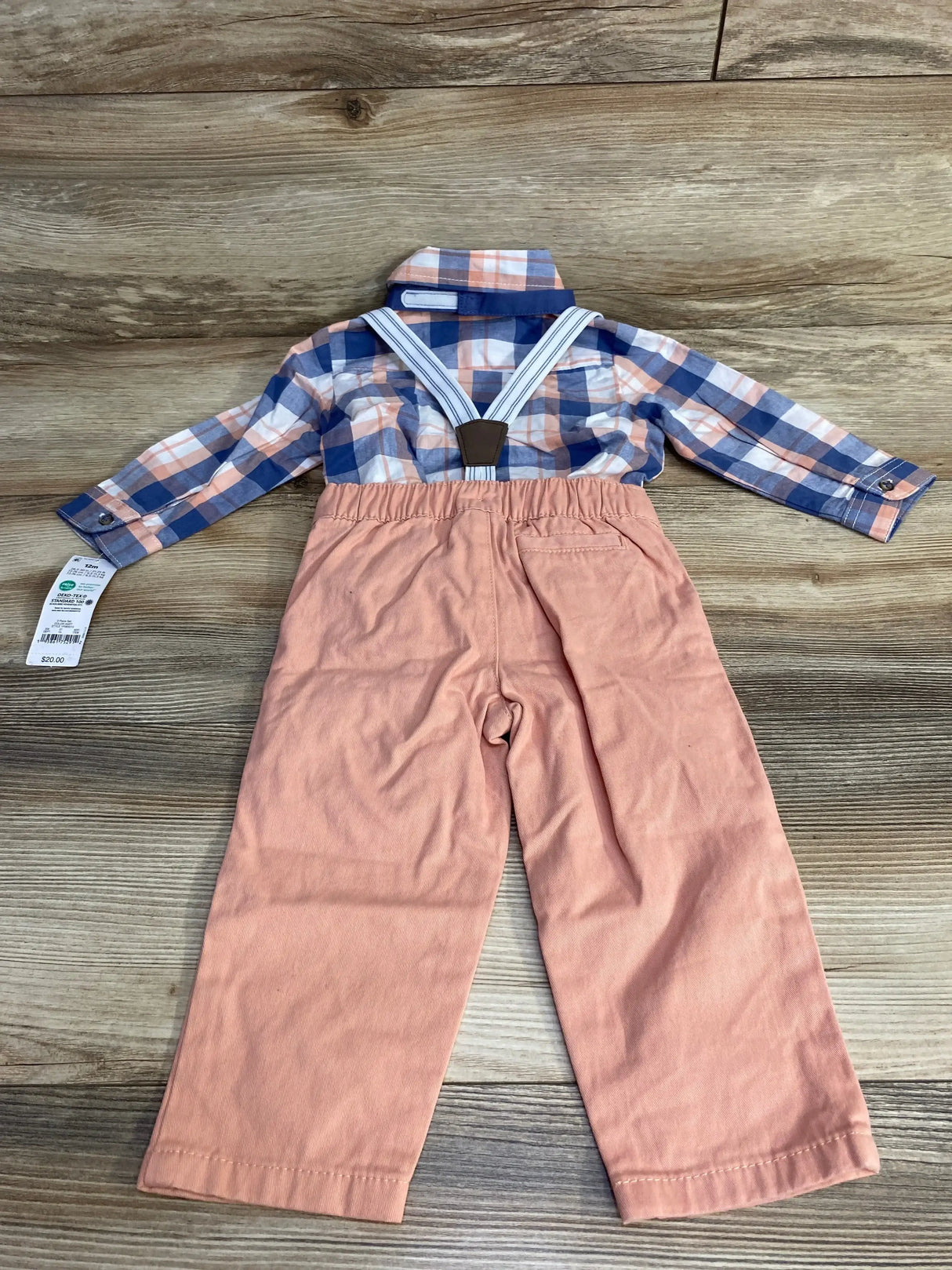 Flat lay of baby blue plaid button up suspender set with pink pants and white striped suspenders on wood floor