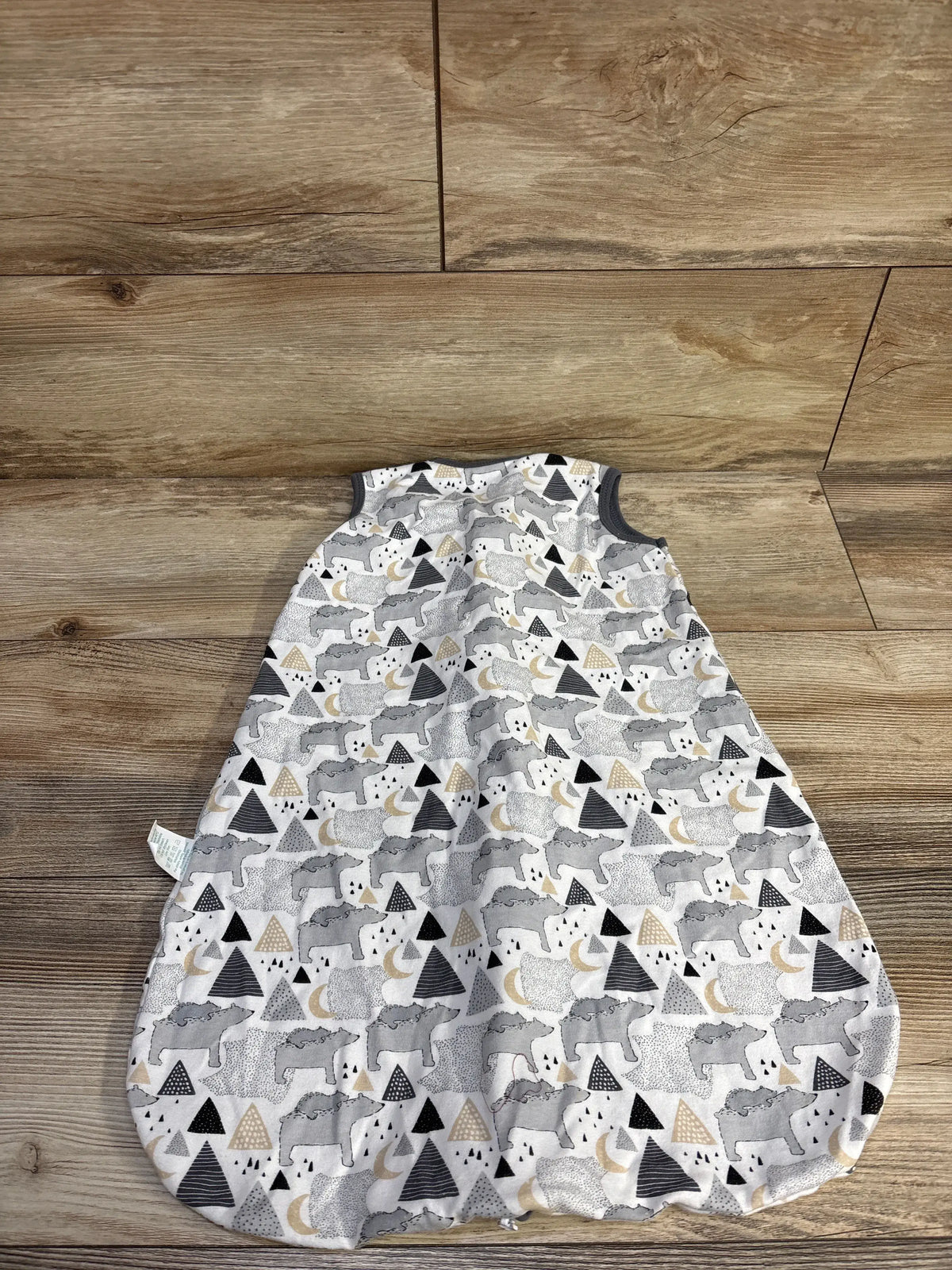 Top view of Cute Castle sleep sack, size 0-6 months, showcasing white cotton fabric with gray, black, and gold animal pattern on a wood floor
