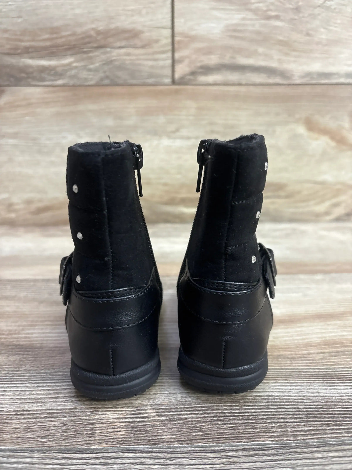 Back view of black toddler boots with zipper and buckle on wooden floor background