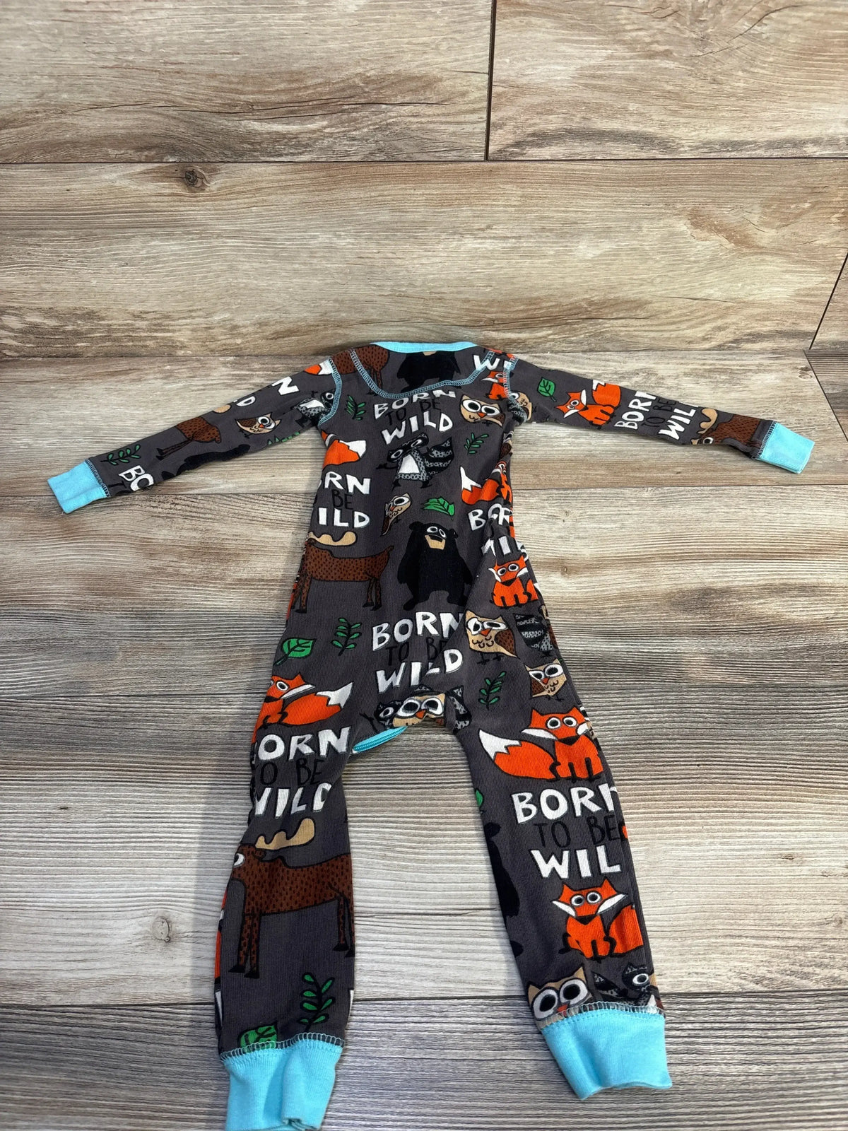 Flat-lay front of Lazy One Born Wild sleeper size 12M showcasing woodland animal print and turquoise cuffs on wood floor