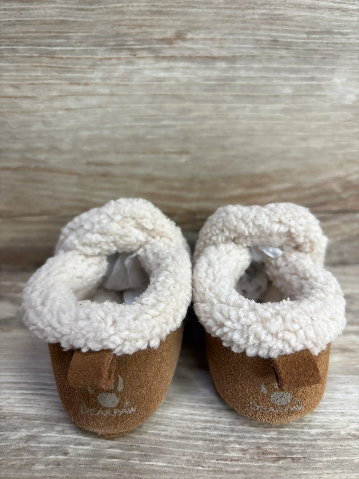 Pair of brown Bearpaw brand baby booties with white fleece lining on wooden surface