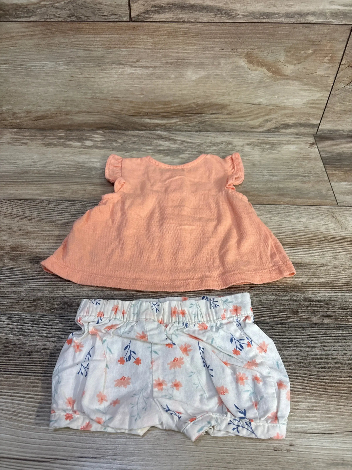 Front view of Just One You 2pc peplum top and shorts set showing coral top and floral shorts with elasticized waist on wood