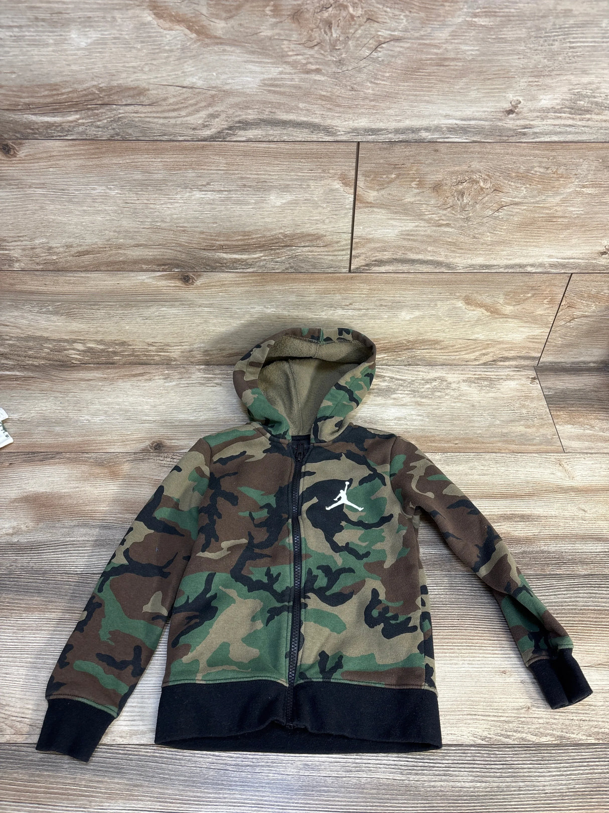 Kids camouflage zip-up hoodie with white Jumpman logo, laid flat on wood floor