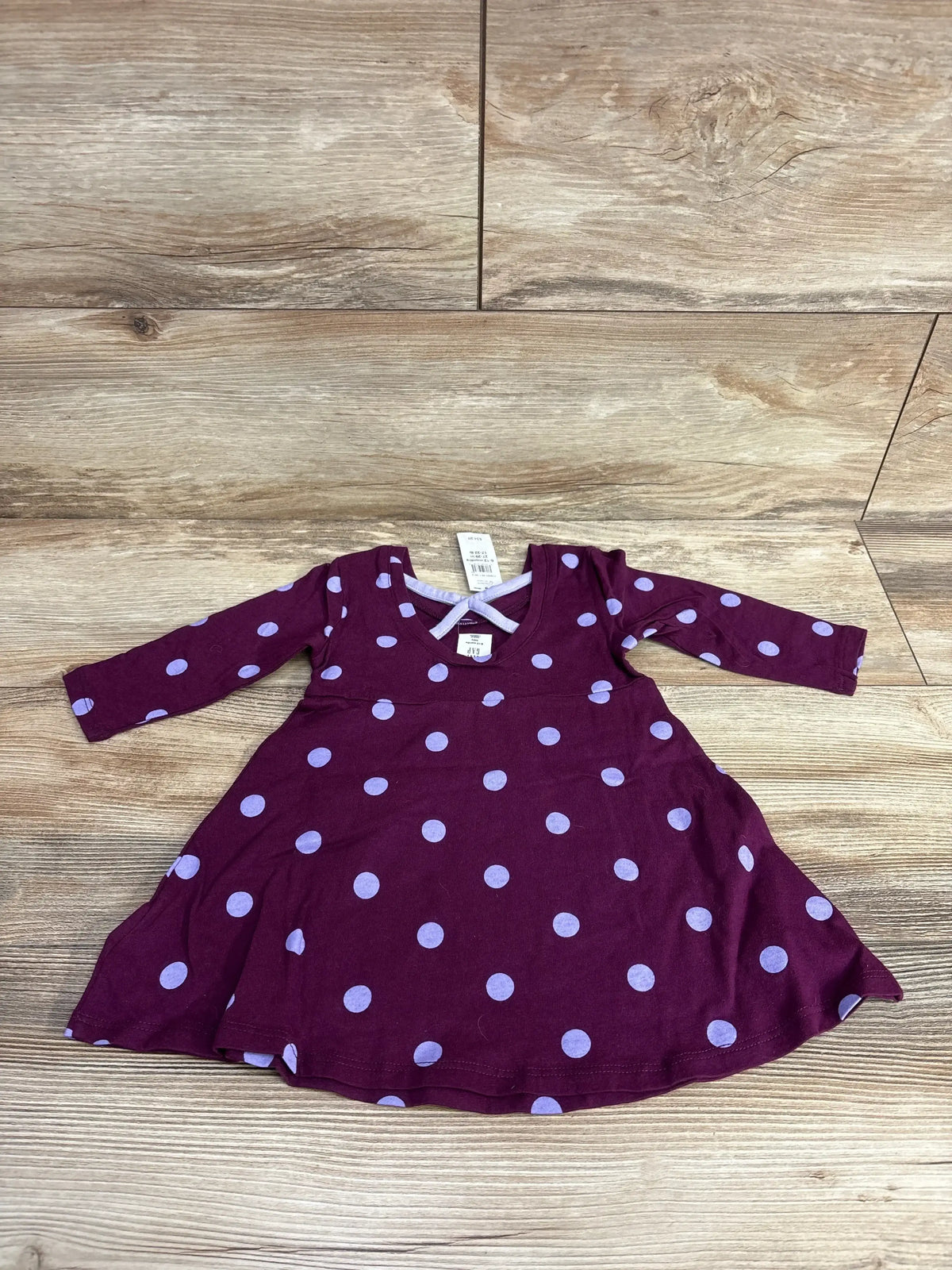 Top-down view of a Baby Gap purple long-sleeve polka-dot cotton dress, size 6 to 12 months, with a flared skirt on wood