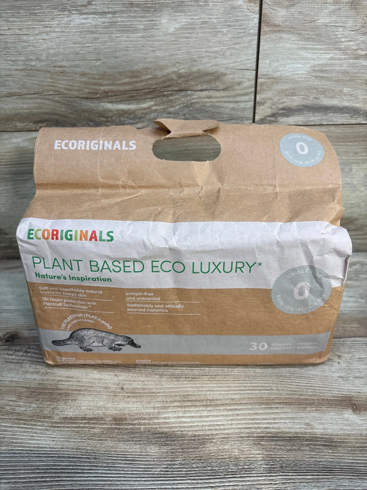 Front view of Ecoriginals plant-based eco luxury size 0 diaper pack showing kraft-paper packaging, unisex size 0 badge, ‘Plant Based Eco Luxury’ text and platypus illustration on wood background