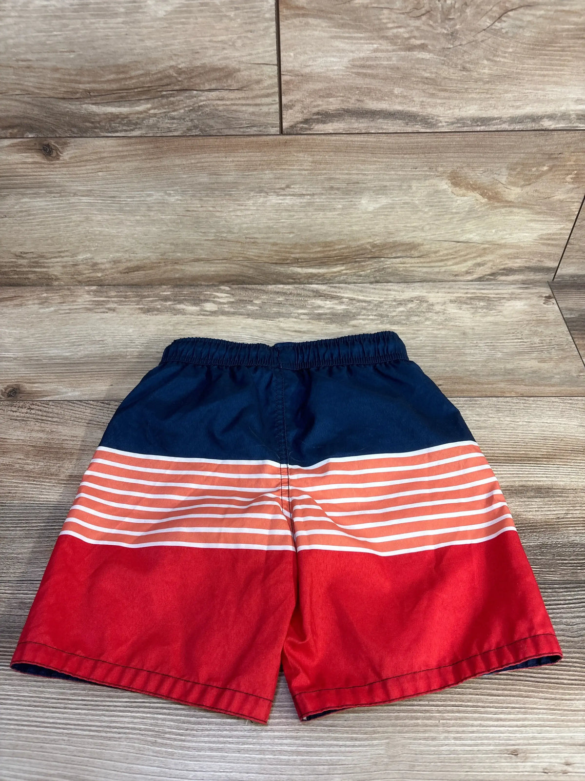 Front view of Marvel Symbol of Truth Captain America swim trunks showcasing navy, red, and white stripes with a wood-grain background
